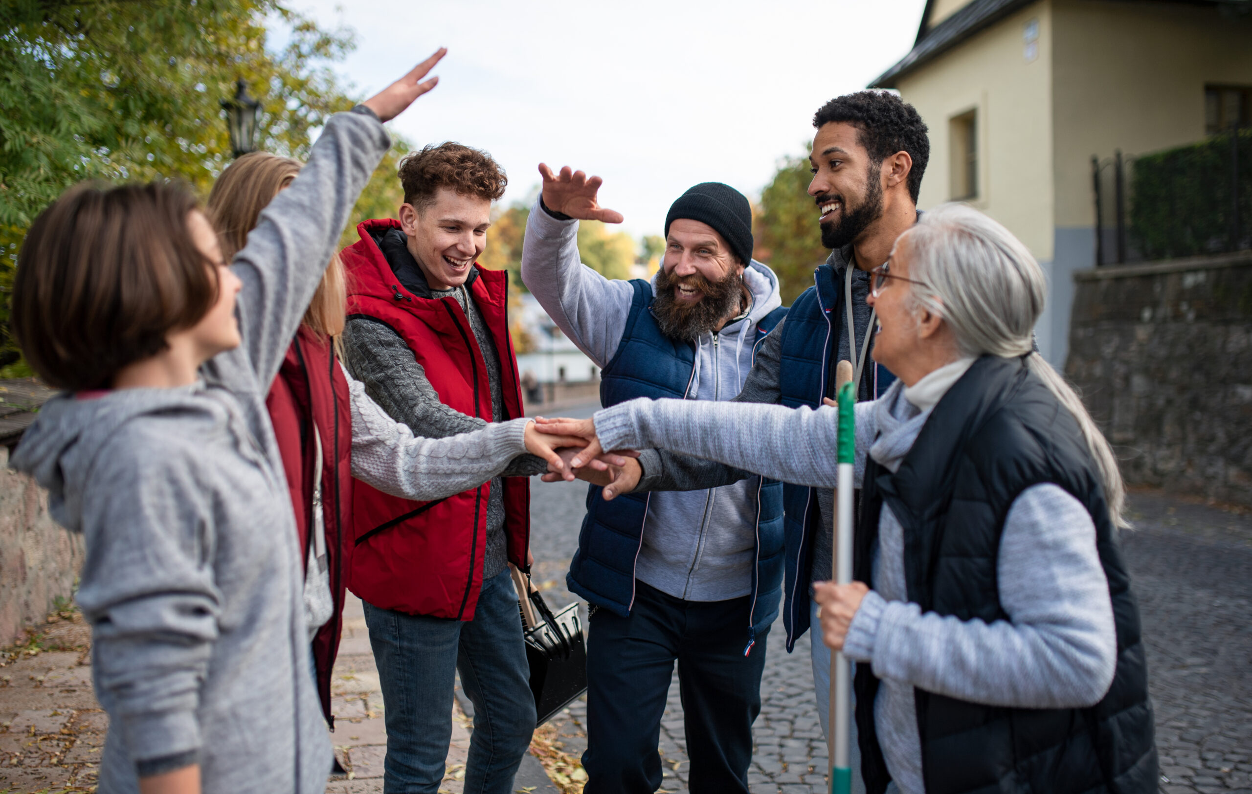 A diverse group of happy community service volunteers stacking hands together outdoors in street